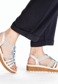 Sandales compensées avec une semelle en liège, des brides métalliques argentées et des embellissements en denim en forme de fleur. Arrière fermé avec un design ouvert à l'avant.