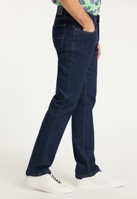 Ciemnoniebieskie dżinsy o prostym kroju, z pięcioma kieszeniami, kontrastowym przeszyciem i gładką teksturą, w połączeniu z białymi sneakersami.