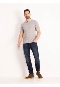 Grijze polo met korte mouwen en een drieknoopsluiting, gecombineerd met donkerblauwe spijkerbroek en bruine veterschoenen. Geweven stof.