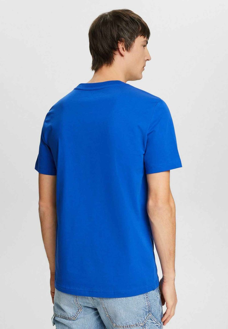 Blå bomullströja med korta ärmar, rund halsringning och rak fåll. Bakstycket visar en enkel design utan några ytterligare detaljer.