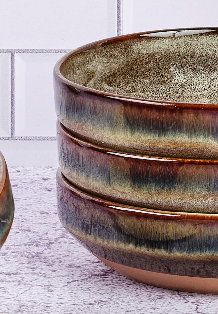 Gestapelte Keramikschalen mit glänzender Oberfläche. Erdtöne in Braun und Grün mit einem strukturierten Rand und glattem Innenraum. Leicht ausladende Form.