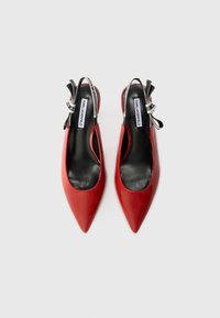 Tacones altos de charol rojo con tiras traseras, puntera en punta, forro interior negro y tiras decorativas con detalle del logo.