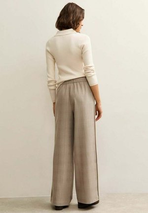 Maglia a maniche lunghe color crema a costine abbinata a pantaloni a vita alta, a gamba larga, a quadri in tonalità beige, caratterizzati da una cintura elastica e dettagli laterali.