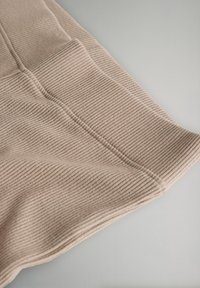 Material bej cu nervuri și suprafață texturată, cu dungi subtile și colț pliat, pe un fundal gri deschis.