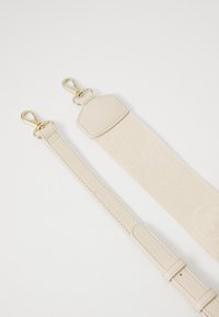 Sangle beige pour épaule en cuir lisse et tissu texturé, longueur ajustable, avec quincaillerie en ton or et motifs décoratifs.