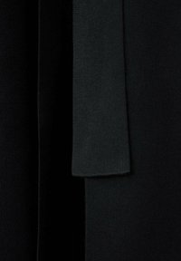 Gros plan d'un tissu noir foncé avec une écharpe ou bande tricotée verticalement drapée dessus, montrant la texture et les couches.