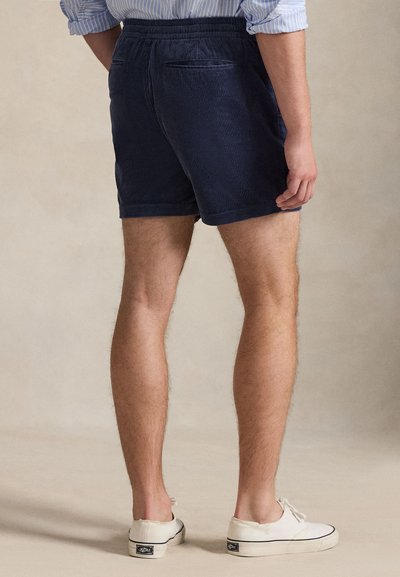 Σορτς από βελούδο κοτλέ σε ναυτικό μπλε, με άνετη εφαρμογή, ελαστική ζώνη μέσης και δύο πίσω τσέπες. Φορεμένα με λευκά αθλητικά παπούτσια, προσφέροντας ένα casual look.