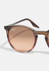 Ochelari de soare cu gradient maro, cu o ramă transparentă din bătut de țestoasă, având lentile rotunde și un logo subtil Ray-Ban pe margine.