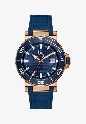 Sinine silikoonist käekell, millel on tekstureeritud tume sinine kelladial, kuldse tooniga aksessuaarid, suured valged tunnimarkerid ja punane sekundinäit. Veekindel kuni 100 m.