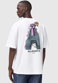 Hvid bomulds-T-shirt med et stort grafisk motiv på ryggen, som viser en lilla næve, en rose og detaljer med pigtråd, mærket med "ALLSAINTS LONDON."