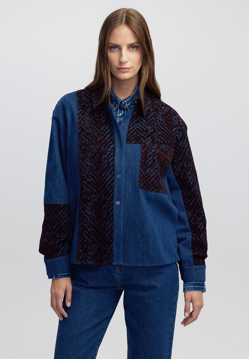 Denim shirt met een donker, gemusterd fluwelen stuk. Heeft een knopenfront, kraag en lange mouwen. Kleurenschema omvat donkerblauw en bordeaux.