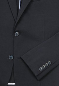 Donker marineblauwe colbert met een nietch lapel, twee voorknopen en een getailleerde pasvorm. De mouw heeft vier decoratieve knopen.