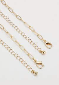 Accessoire en chaîne dorée avec des styles de maillons variés, présentant une texture lisse, une quincaillerie de fermeture, et des accents en forme de boule arrondie.