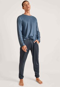 Blauwe lange mouw top met een ontspannen pasvorm, gecombineerd met donkerblauwe taps toelopende joggers met een elastische tailleband en zijzakken. Glad stoftextuur.