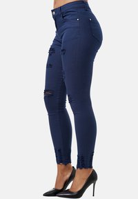 Jeans ajustados de mezclilla azul marino con detalles desgastados en las rodillas y dobladillo deshilachado. Presenta una cintura clásica y bolsillos traseros.