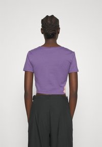 Fioletowa, krótkoterminowa koszulka z bawełny, z krótkimi rękawami i okrągłym dekoltem. Posiada akcentujący wzór z boku. Połączona z ciemnymi, luźnymi spodniami.