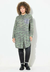 Groene gestreepte shirtjurk met tegen knoopsluiting en een paillettenzak aan de linkerkant. Gecombineerd met zwarte jeans met opgerolde mouwen en enkellaarzen.