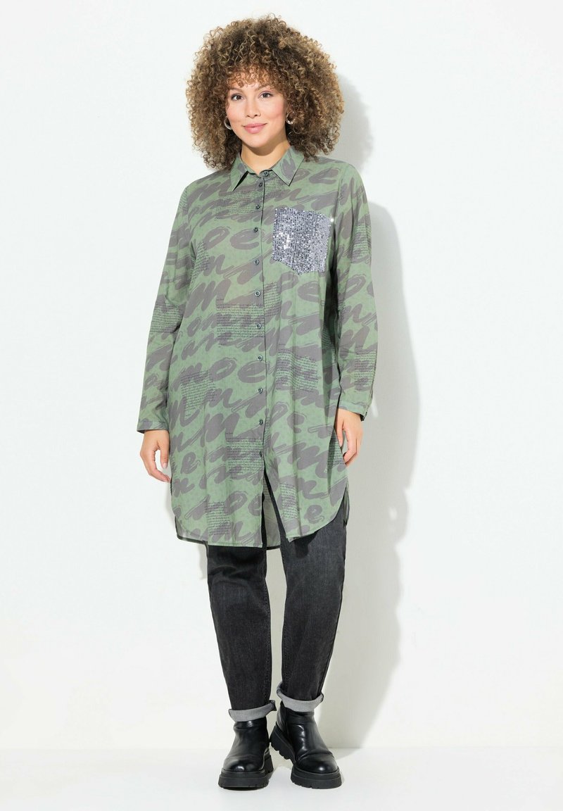 Groene gestreepte shirtjurk met tegen knoopsluiting en een paillettenzak aan de linkerkant. Gecombineerd met zwarte jeans met opgerolde mouwen en enkellaarzen.