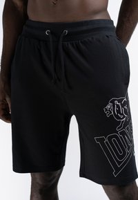 Shorts de sport noirs en tissu mélangé coton, avec une taille élastiquée à cordon de serrage et un grand logo graphique blanc sur la cuisse gauche.
