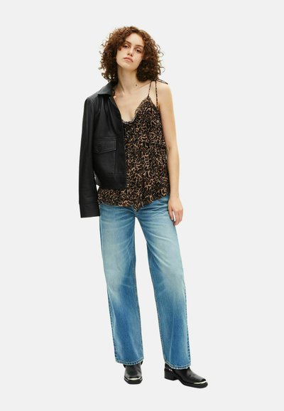 Veste en cuir noire sur un haut sans manches à motifs marron, associée à un jean large bleu clair et des bottines noires avec des accents en argent.