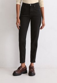 Czarne jeansy typu high-rise z dopasowanym krojem, z kieszeniami z przodu, kontrastowym szwem oraz zużytymi brązowymi butami na sznurówki z masywną podeszwą.