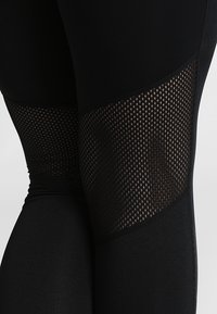 Černé legíny s síťovinou po stranách, s hladkým povrchem a přiléhavým střihem, který tvaruje nohy.