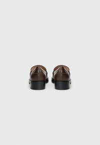 Brown leather shoes with a smooth texture, a closed-back design, and block heels; minimalistic detailing on the upper.