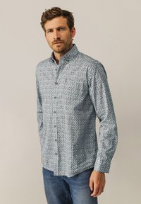 Button-up-Hemd in hellblau mit grünem Blumenmuster, langärmlig, mit klassischem Kragen, kombiniert mit blauen Jeans.