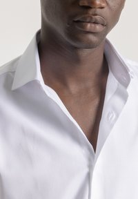 Primer plano de la parte inferior de la cara y el cuello de un hombre que lleva una camisa de vestir blanca con los botones superiores desabrochados.