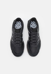 Zapatillas deportivas negras hechas de malla y ante, con una superficie texturizada, rayas blancas y una plantilla estampada. Los cordones son negros con puntos blancos.