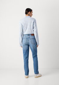 Lichtblauw gestreepte, langarms pullovershirt gecombineerd met vervaagde blauwe rechte jeans en witte sneakers. Patchlabel op de achterkant van de jeans.