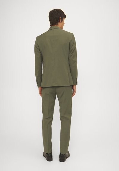 Herrenanzug aus olivgrünem Stoff, einreihige Jacke mit spitzem Revers, slim-fit Hose und schwarzen Schuhen, von hinten gezeigt.