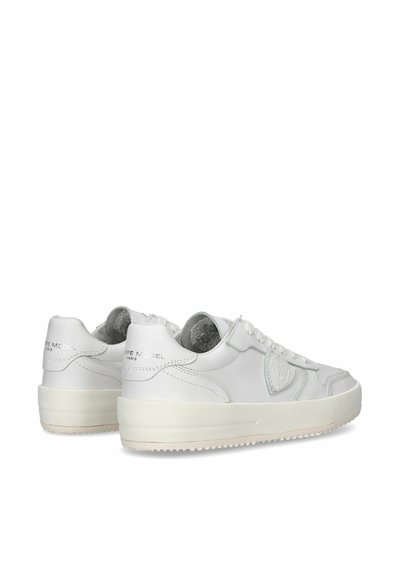 Baskets en cuir blanc avec une texture lisse, languette rembourrée et branding subtil sur le talon. Semelle en caoutchouc plate, légèrement surélevée.