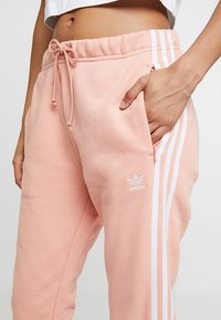 Rosa sweatpants med elastisk midjeband, snörning, sidofickor och vita tre-stripes detaljer; har en liten vit logotyp på låret.