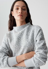 Grauer strukturierter Pullover mit hohem Kragen, ausgestattet mit einem geschlungenen Stoffdesign und gerippten Bündchen. Weiches, kuscheliges Material.