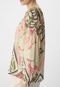 Bluzka w kwiatowy wzór w odcieniach zieleni, różu i brązu. Długie rękawy z marszczeniami; lekki materiał i luźny krój.