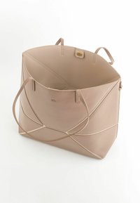 Leren draagtas in zacht beige met een geometrisch ontwerp. Voorzien van twee handvatten en een drukknoopsluiting. Gladde textuur met zichtbare stiksels.