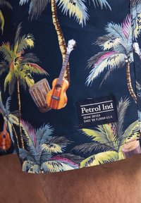 Tmavě modré plavky s tropickým motivem, na kterém jsou palmy, kytary a buben. Součástí je tkaná značka na lemu.