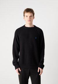 Pulover negru din tricot cu model cu un guler rotund și un logo albastru pe piept. Are mâneci lungi și o țesătură texturată.
