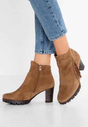 Braune Wildleder-Stiefeletten mit klobigen Absätzen, seitlichem Reißverschluss und Fransen-Detail, getragen zu hochgekrempelten blauen Jeans.