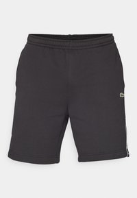 Črne športne hlače iz mehke tkanine, ki imajo elastičen pas, stranske črte in majhen vezen logotip na sprednji strani.