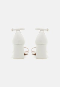 Sandales blanches à talon haut avec un talon épais, une bride de cheville, un design ouvert sur le devant et une texture lisse. Style minimaliste avec une couleur unie.