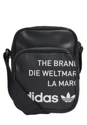 Czarna torba na ramię Adidas z regulowanym paskiem, przednią kieszenią na zamek i białym częściowym tekstem po angielsku, niemiecku i francusku.