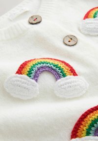 Tissu blanc avec des patchs arc-en-ciel colorés au crochet et deux boutons ronds en bois cousus sur la surface.