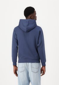 Marineblå hoodie med et lagdelt design, der har en stor hætte, lange ærmer og en ribbet kant. Bagsiden er glat uden mønstre eller accenter.