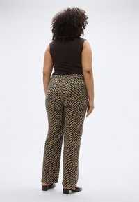 Top marrone senza maniche abbinato a pantaloni svasati con motivo a strisce zebrato in marrone chiaro e nero. Vista posteriore mostra le tasche sul retro.