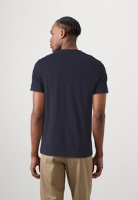 Camiseta de algodón azul marino, de manga corta, con cuello redondo, textura suave, corte relajado, vista desde la parte de atrás sobre un fondo liso.