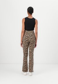 Crni rebrasti top bez rukava, hlače sa zvonastim nogavicama u leopard uzorku s visokim strukom i bijele tenisice, prikazano sa stražnje strane na bijeloj pozadini.