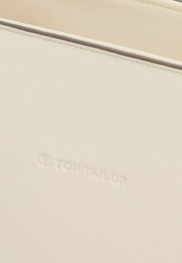 Helle beige synthetische Geldbörse mit glatter Oberfläche, mit erhobener Prägung "TOM TAILOR." Einfaches Design, keine sichtbaren Hardware-Elemente oder Akzente.