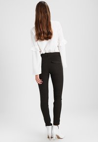 Svarta figurnära byxor med bakfickor, tillsammans med en vit blus med volanger vid ärmarna, och vita klackiga ankelskor.